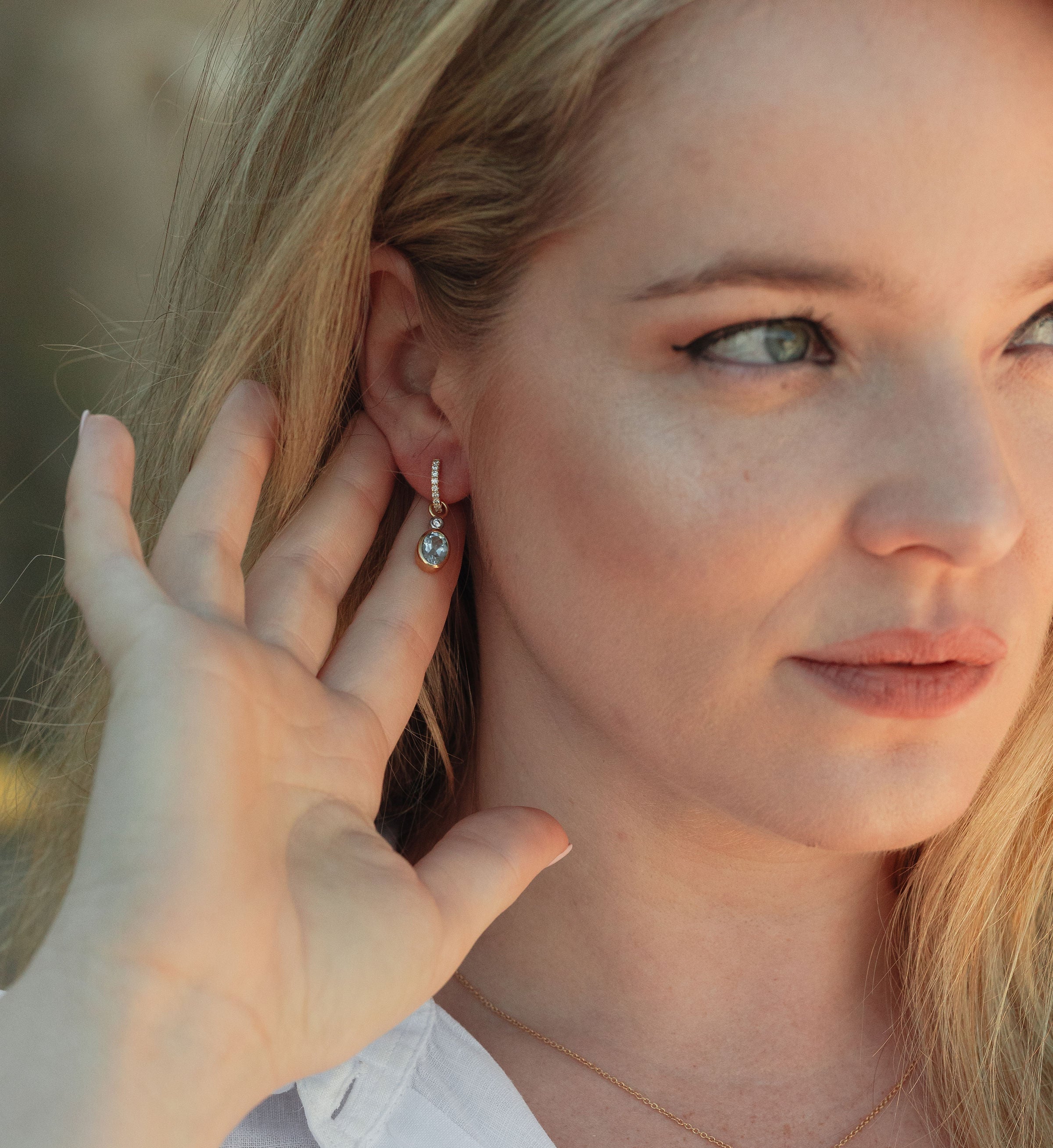 Woman wearing LUNA 18ct gold and diamond earrings with blue topaz and diamond attachments