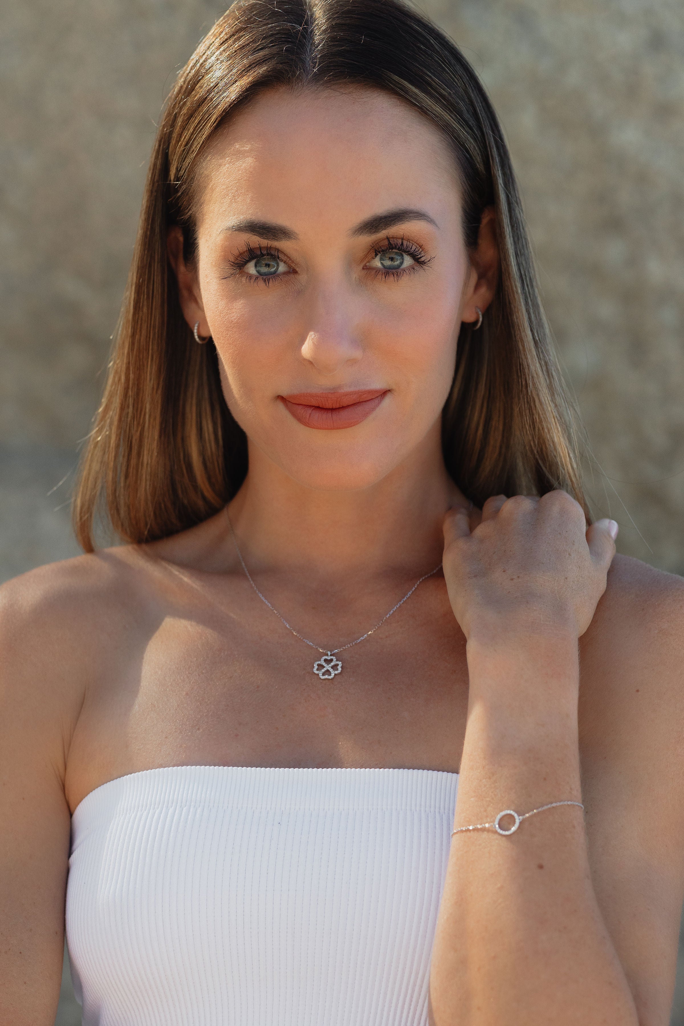 Woman wearing a LUNA gold and diamond pendant, gold and diamond huggie earrings and diamond bracelet against a neutral background